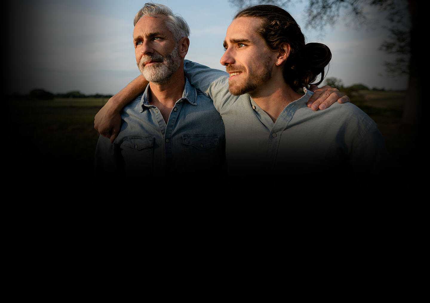 Un hombre mayor y su hijo adulto, uno junto al otro, con los brazos en los hombros del otro