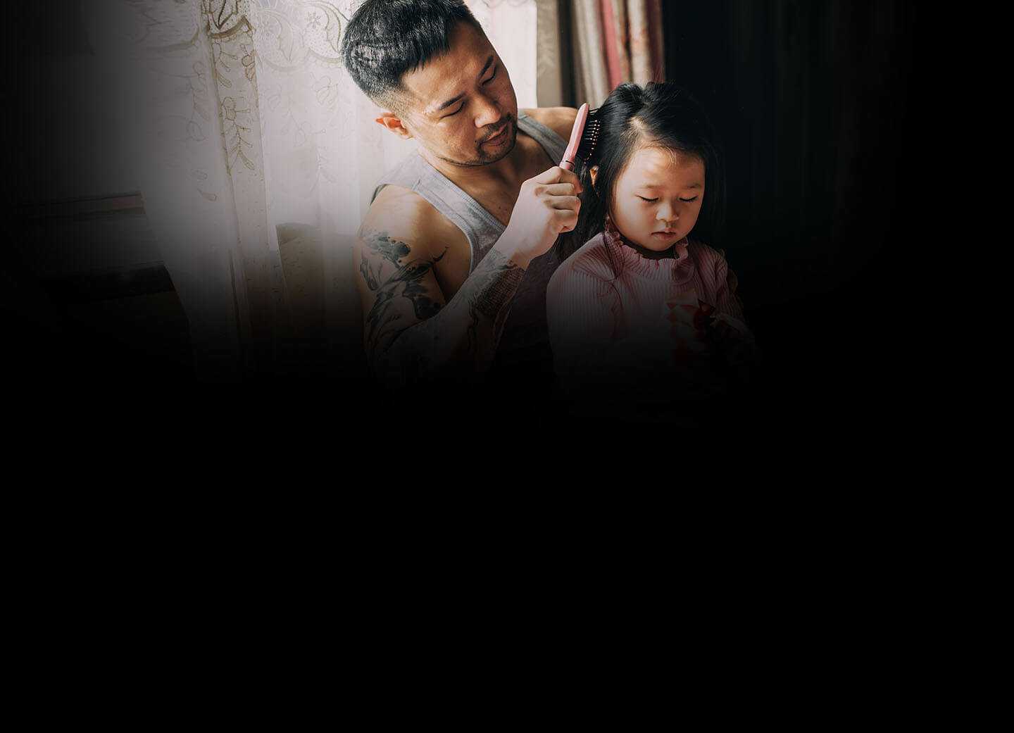 Un padre peina el cabello de su hija junto a una ventana