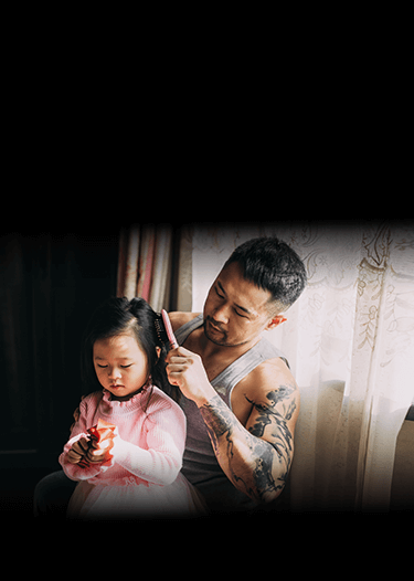 Un padre peina el cabello de su pequeña hija junto a una ventana, imagen invertida