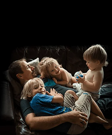 Dad with three kids laughing on a couch